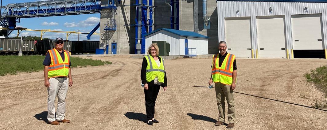 three people in reflective yellow vests standing in front of grain elevator